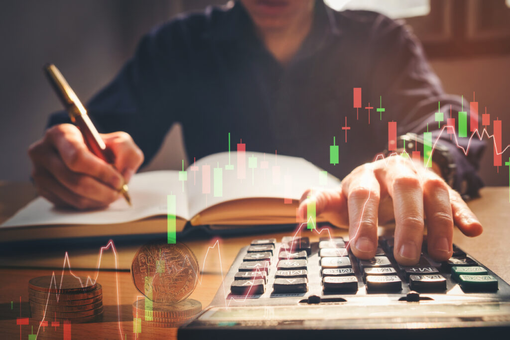 double exposure business man using calculator and writing business plan at workplace,man holding pens and making notes trading graph of stock market