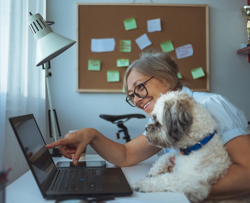 Woman smiling, holding dog, and pointing to laptop