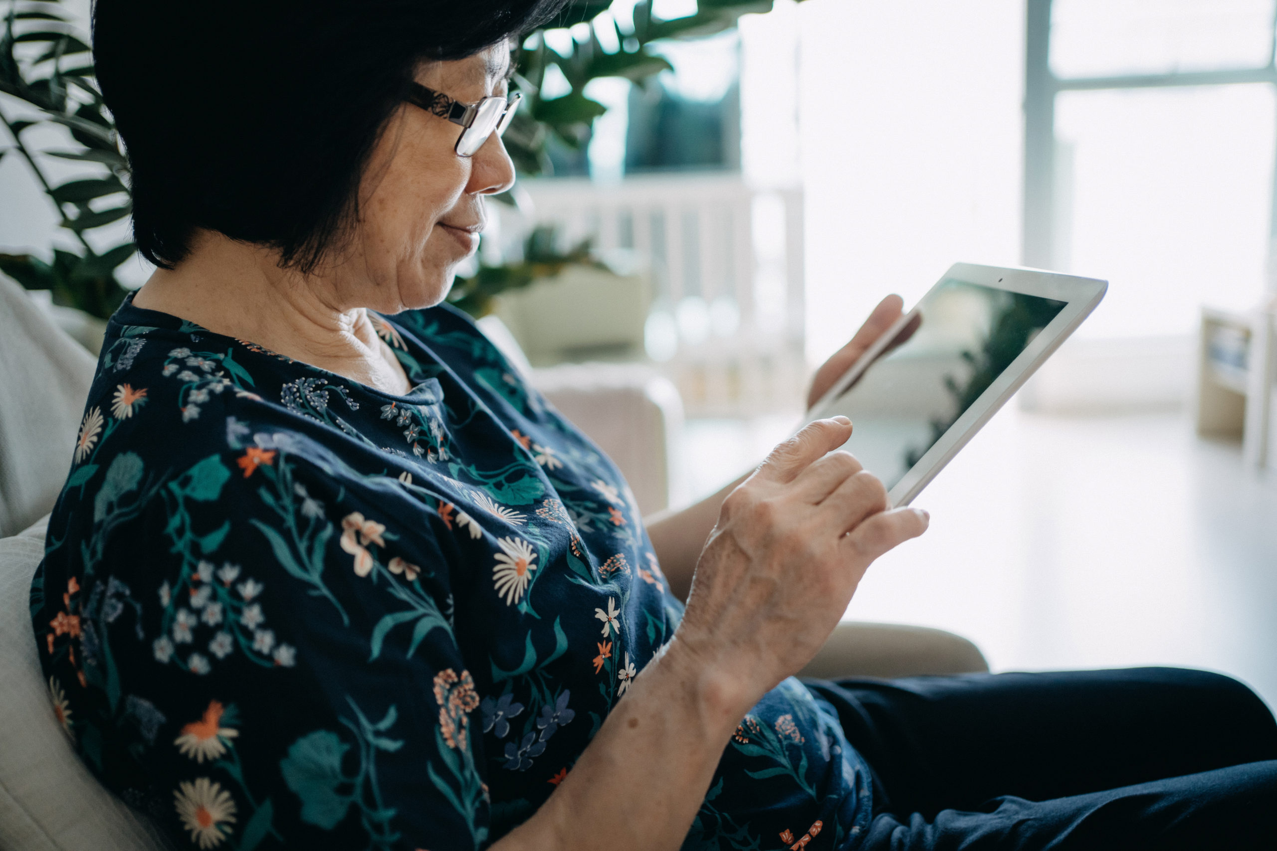 Senior Asian woman using digital tablet while relaxing on the sofa in the living room at home